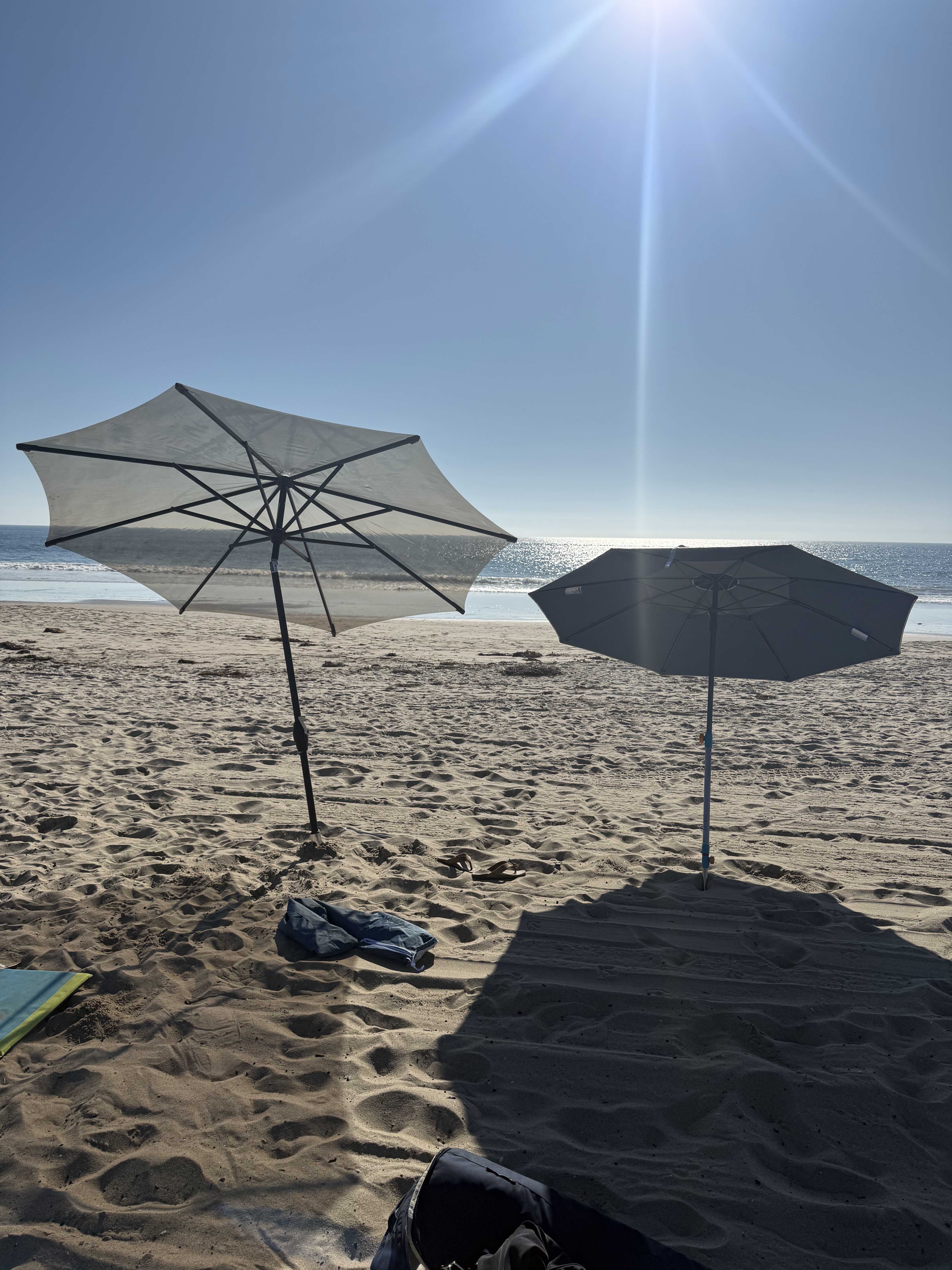 Two beach umbrellas on a sandy beach with a clear blue sky.